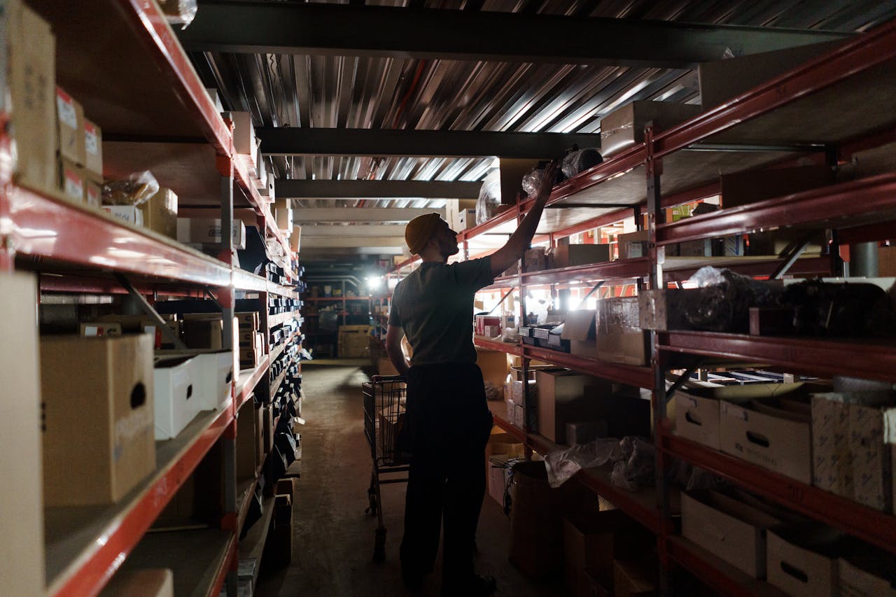 A worker arranging inventory on shelves in a dimly lit warehouse, utilizing efficient storage practices.
